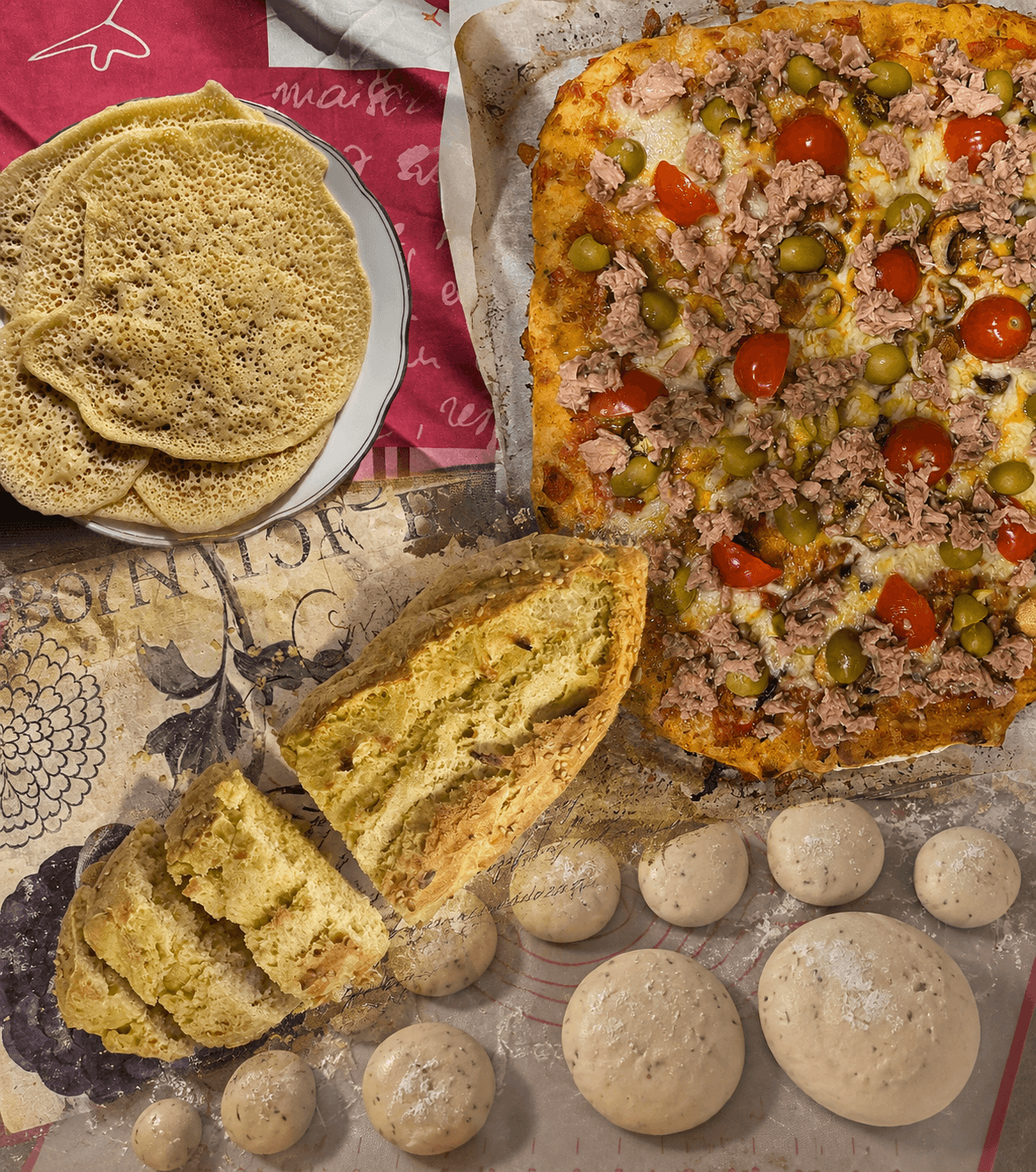 A collage of home baking: baghrir pancakes, a tuna pizza, sliced yellow bread, and dough balls on a mat.